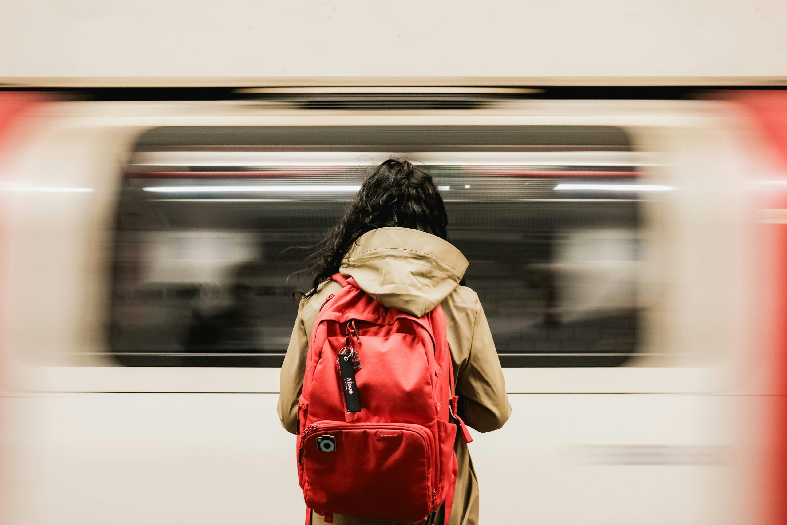 A person with a red backpack waiting as a train speeds past in the London Underground.